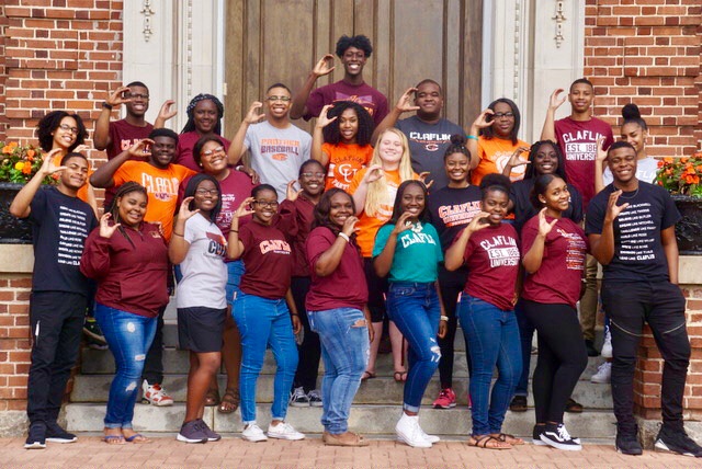 Thalia and classmates in a group smiling at the camera and making a C with their hands.